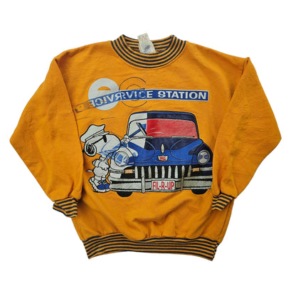 A vintage Peanuts Snoopy sweatshirt with a graphic of Snoopy working at a service station, wearing a gas station attendant uniform, and a car with the text 'Fill-R-Up'. The shirt is yellow with a striped collar and the print has silver glitter detail.